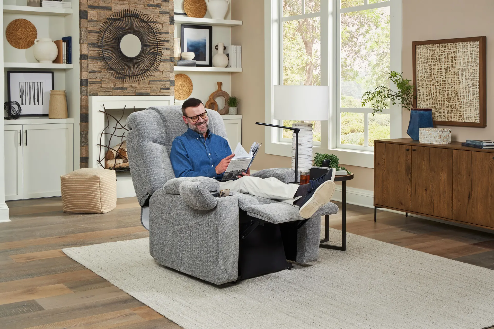 A man reading in an UltraComfort Venice power lift recliner in Slate, reclined beside a fireplace